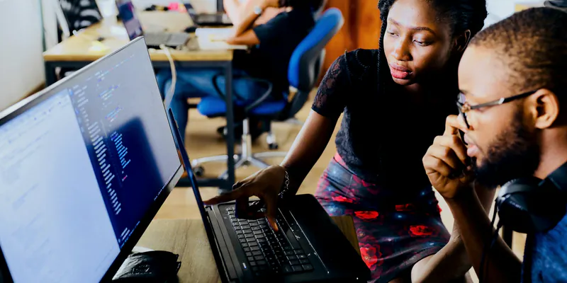 Deux ingénieurs examinent du code sur un ordinateur portable, dans un open space.