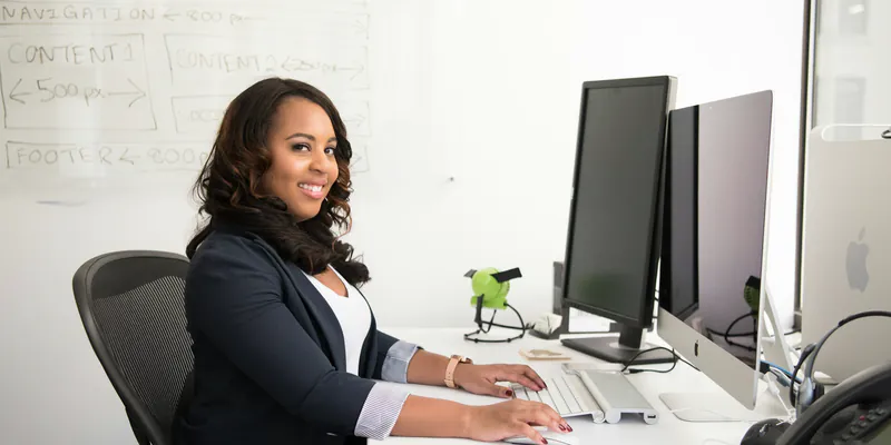 Une professionnelle sourit devant son poste de travail, dans un bureau lumineux.